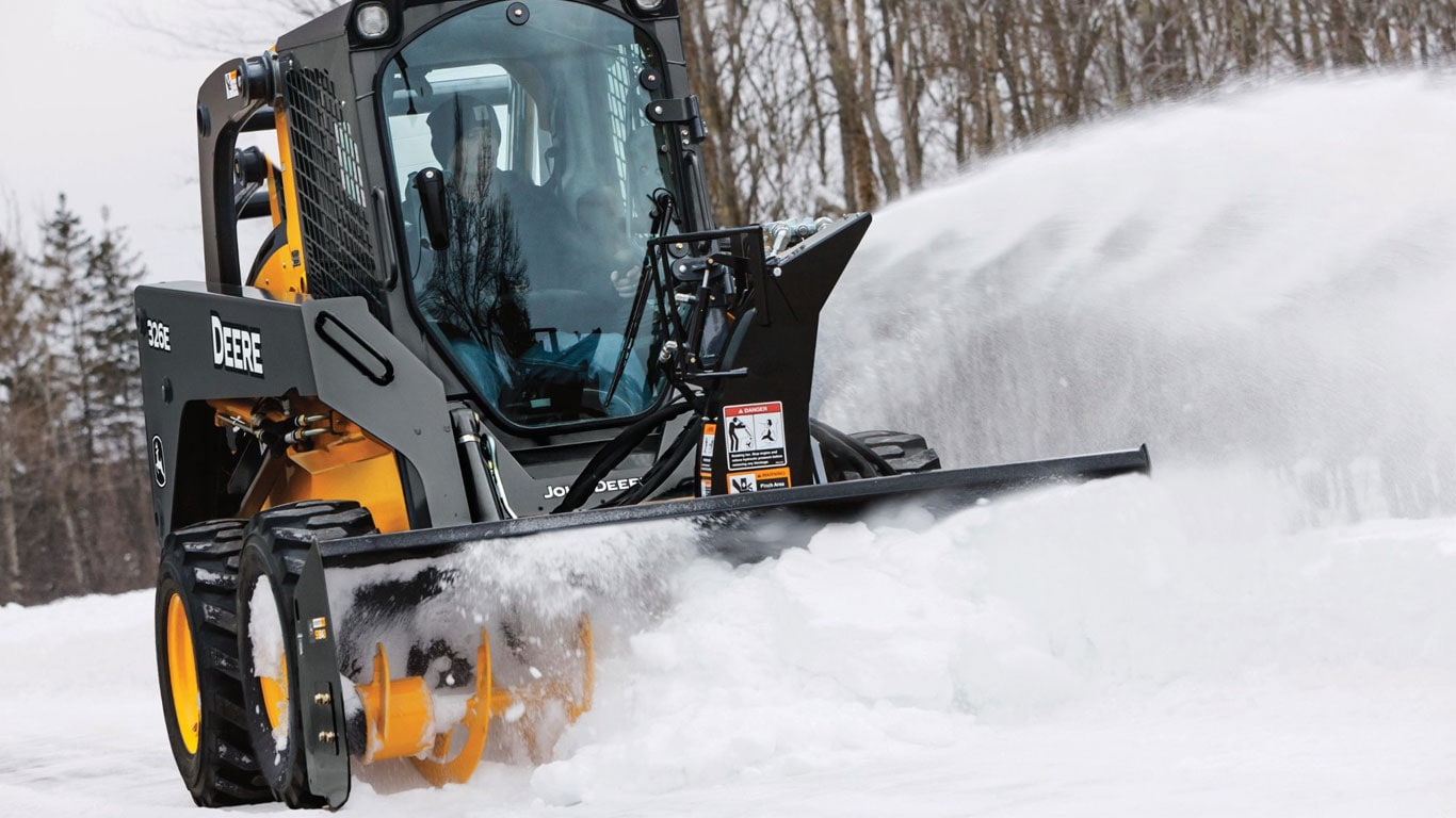 Skid steer with snow blower attachment moving snow.
